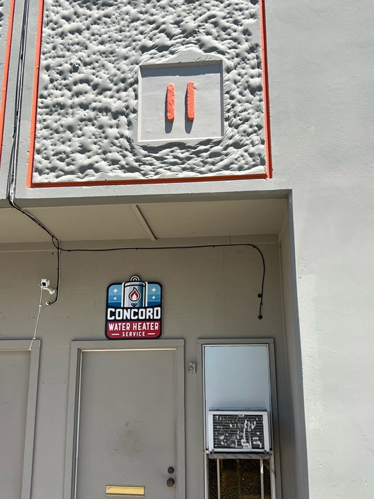 Concord Water Heater Service storefront entrance with company sign and logo visible beneath overhead lighting fixture.